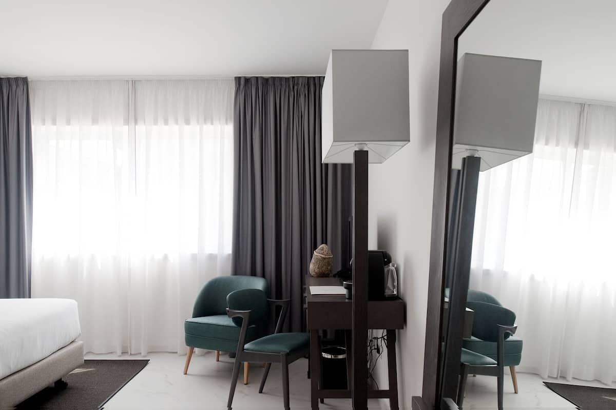 Una habitación de hotel con una cama, dos sillas, un escritorio, una lámpara y un espejo.