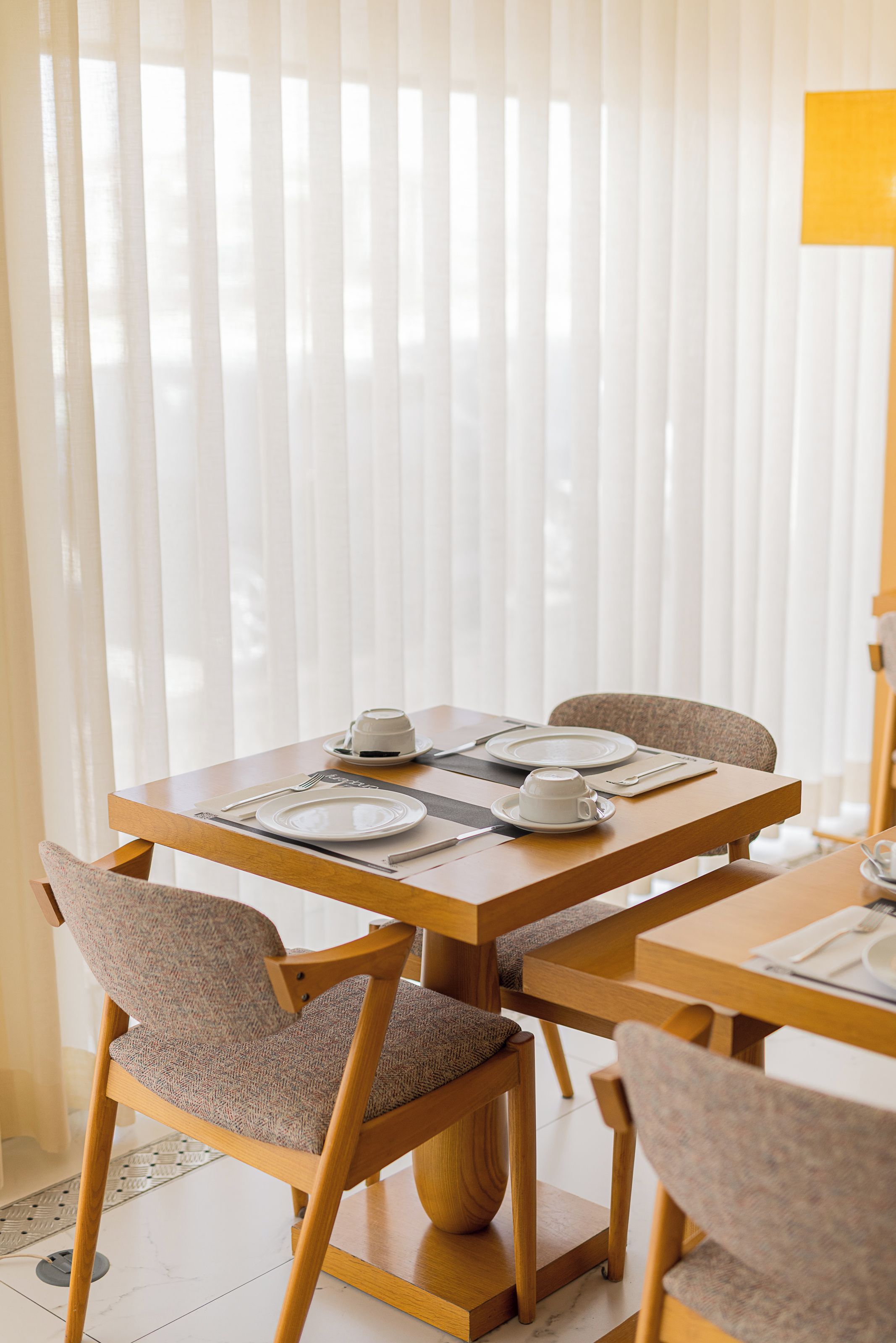 A dining area with a table set for two, chairs, and a window with blinds.