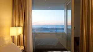Habitación de hotel con cama, mesita de noche, lámpara y vista al océano a través de un ventanal.