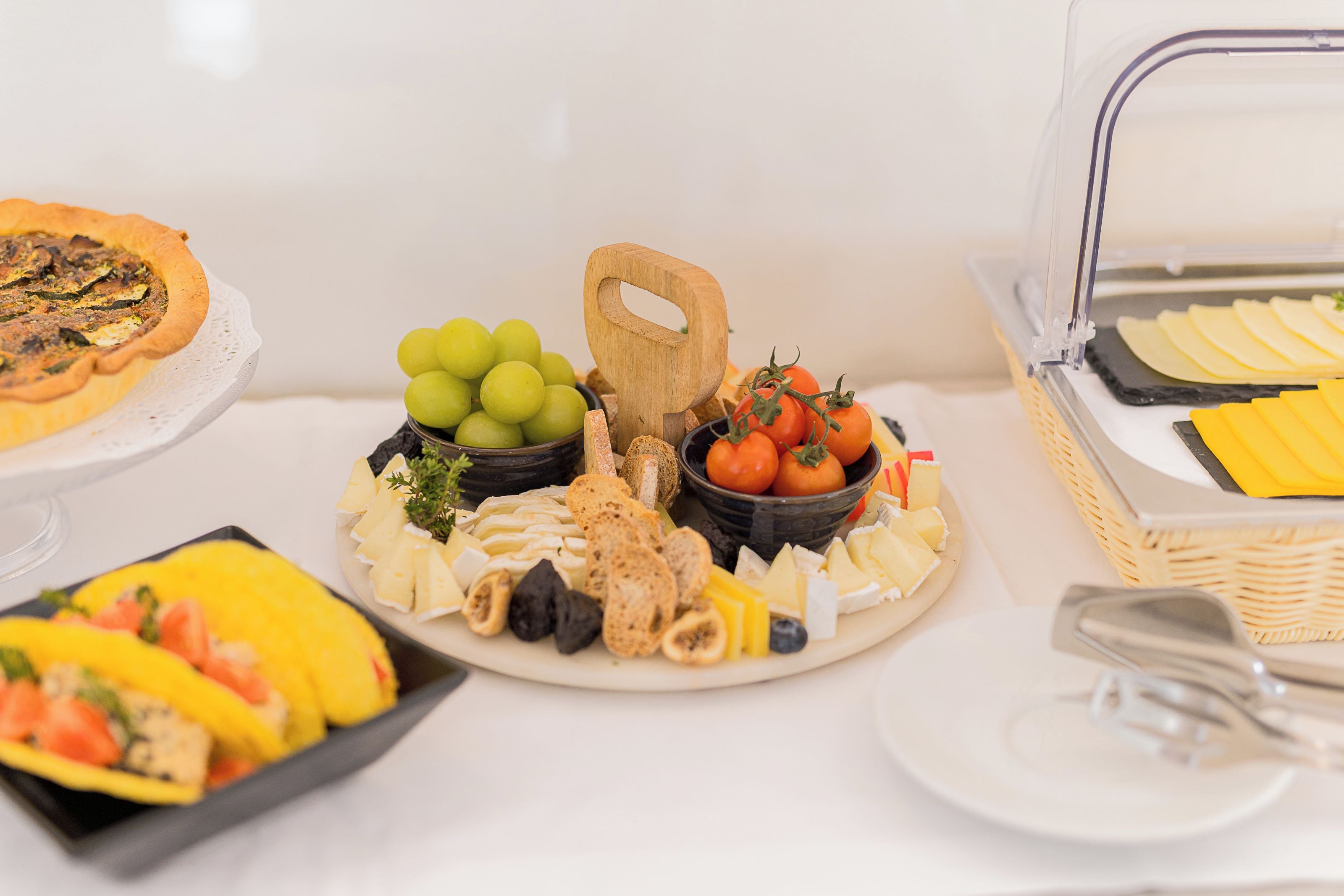 Une table de buffet proposant divers plats, notamment une quiche, du fromage, des fruits et du pain.