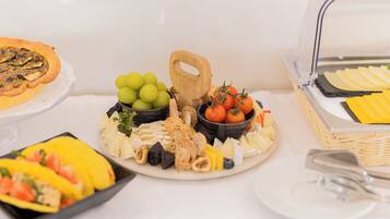 Une table de buffet proposant divers plats, notamment une quiche, du fromage, des fruits et du pain.