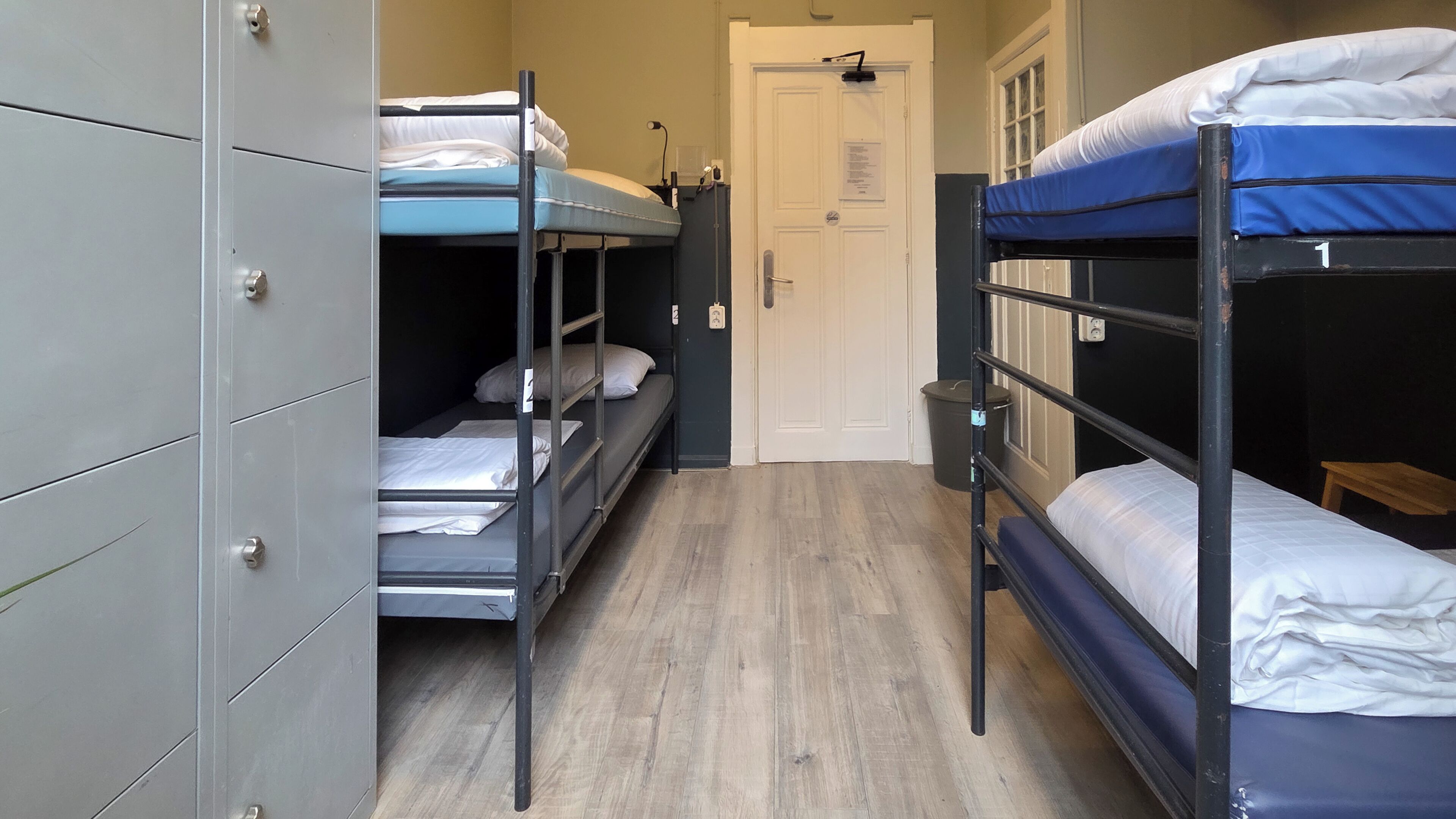 A dormitory room with bunk beds, a wardrobe, and a door.