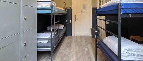 A dormitory room with bunk beds, a wardrobe, and a door.