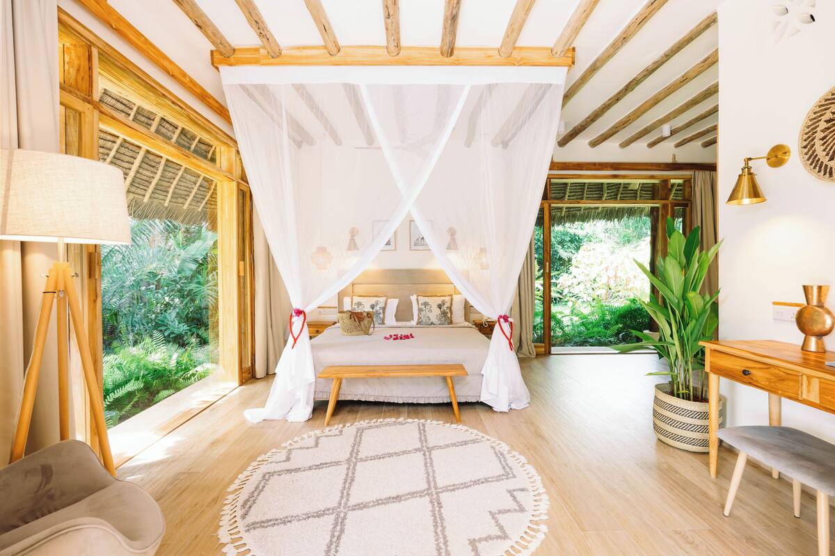 Un dormitorio con cama con dosel, suelo de madera, alfombra redonda, un escritorio y una planta en maceta.