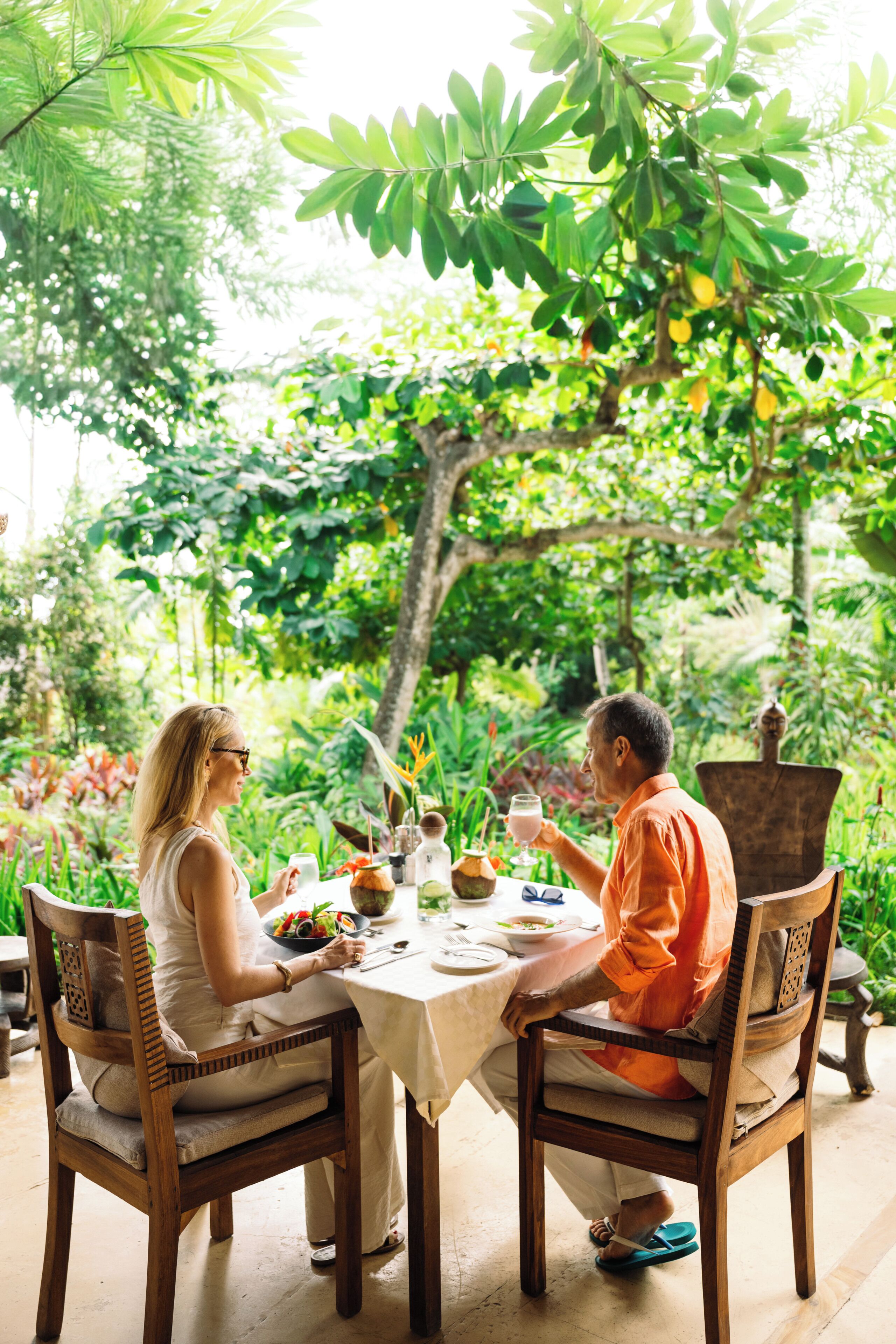 A dining table with chairs, surrounded by lush greenery and a tree.