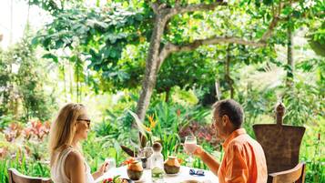 A dining table with chairs, surrounded by lush greenery and a tree.