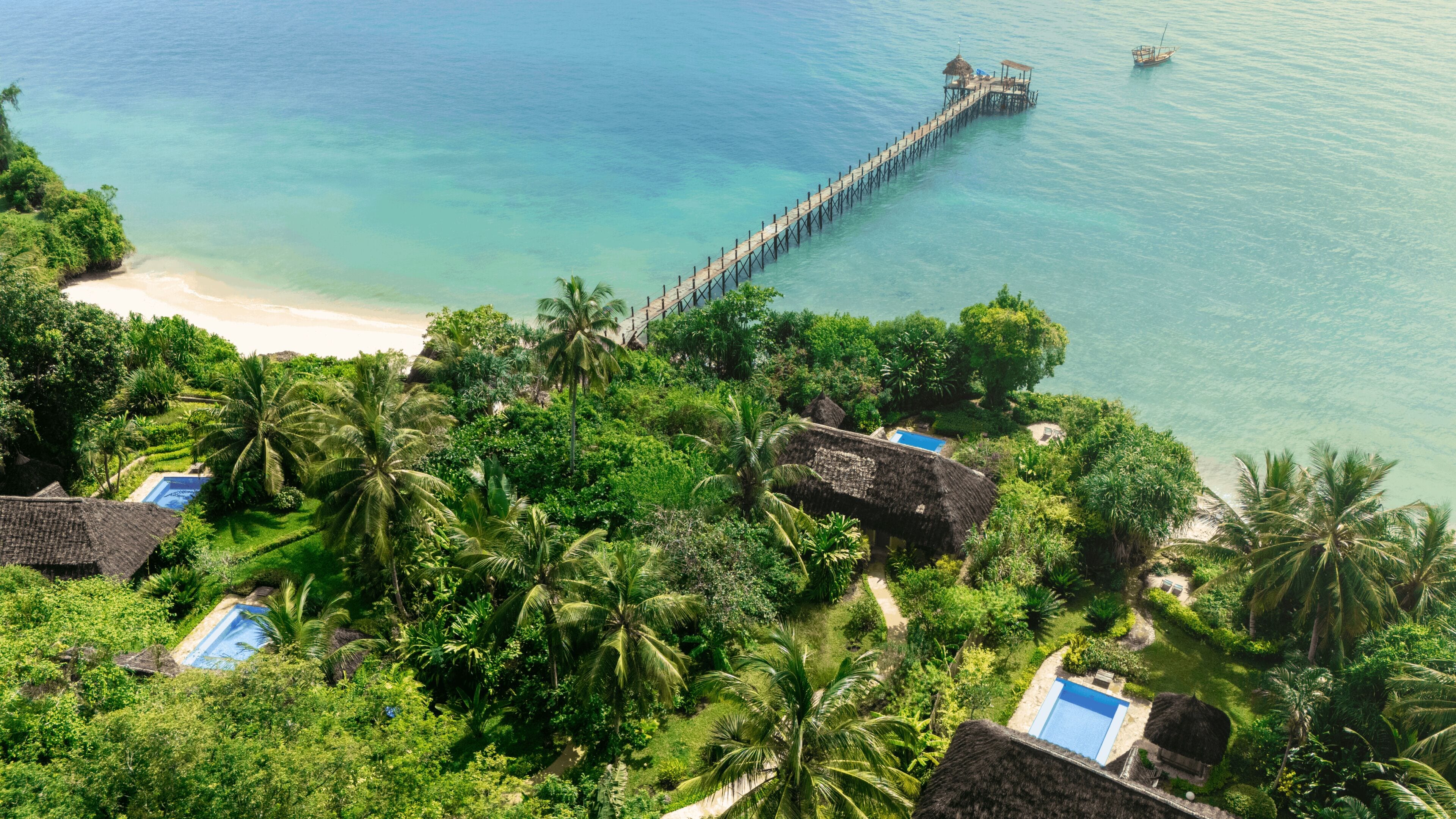 A tropical resort with a long pier extending into the sea, surrounded by lush greenery and palm trees.