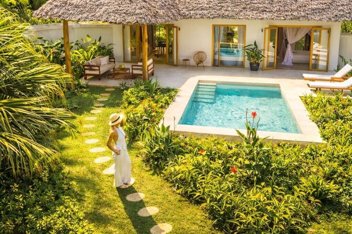 Un resort con piscina, edificios de techo de paja y abundante vegetación.