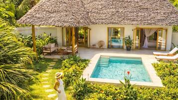 Un resort con piscina, edificios de techo de paja y abundante vegetación.