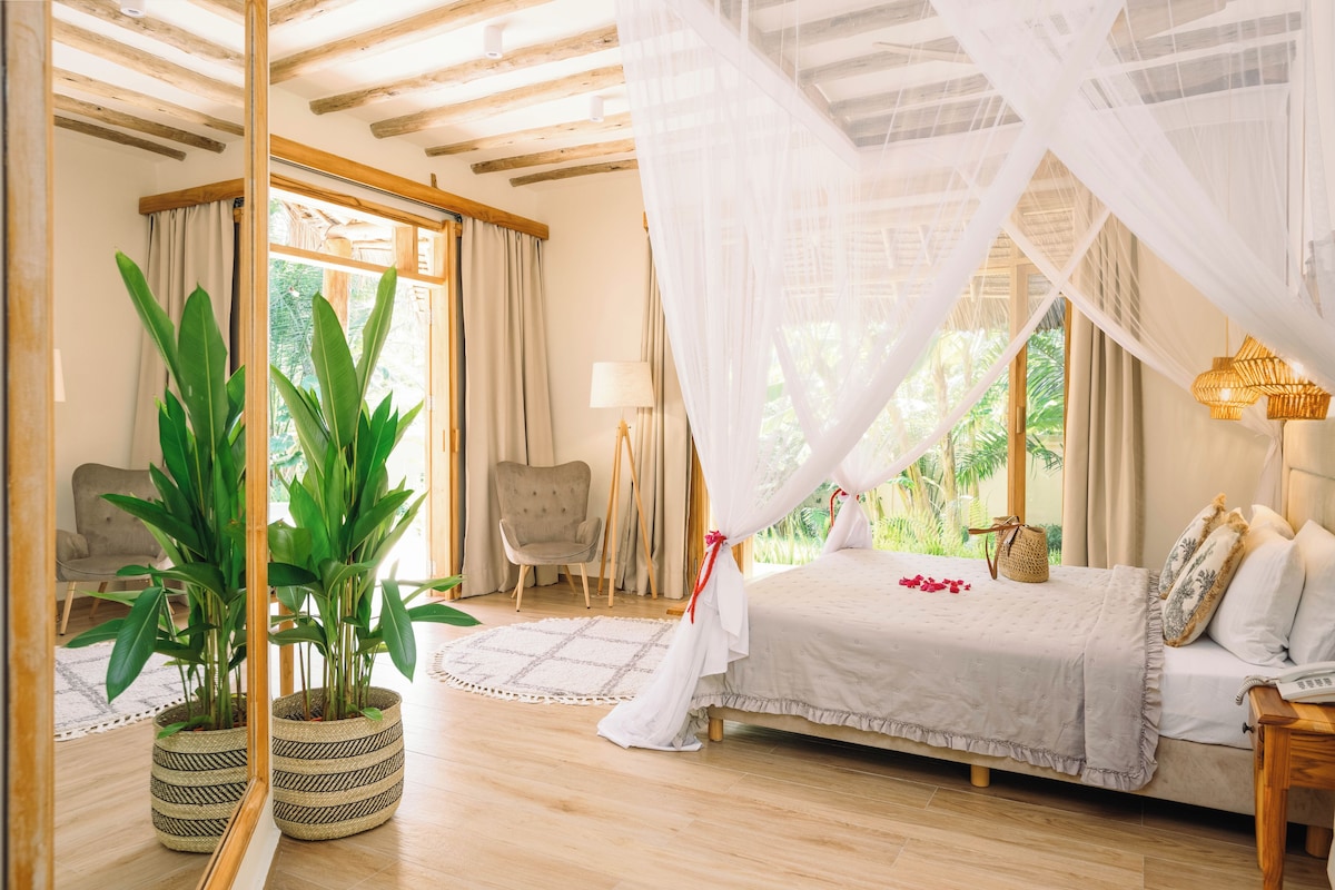 A bedroom with a bed, bedside table, lamp, and potted plants.