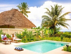 A poolside area with a thatched-roof structure, palm trees, and a clear view of the ocean. - Zanzi Resort (Kama)