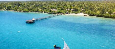 A boat on turquoise water with a pier extending into the sea, surrounded by dense green foliage.