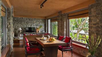 A spacious room with a stone wall, a wooden dining table, red chairs, a TV, and a large window with a view of greenery.