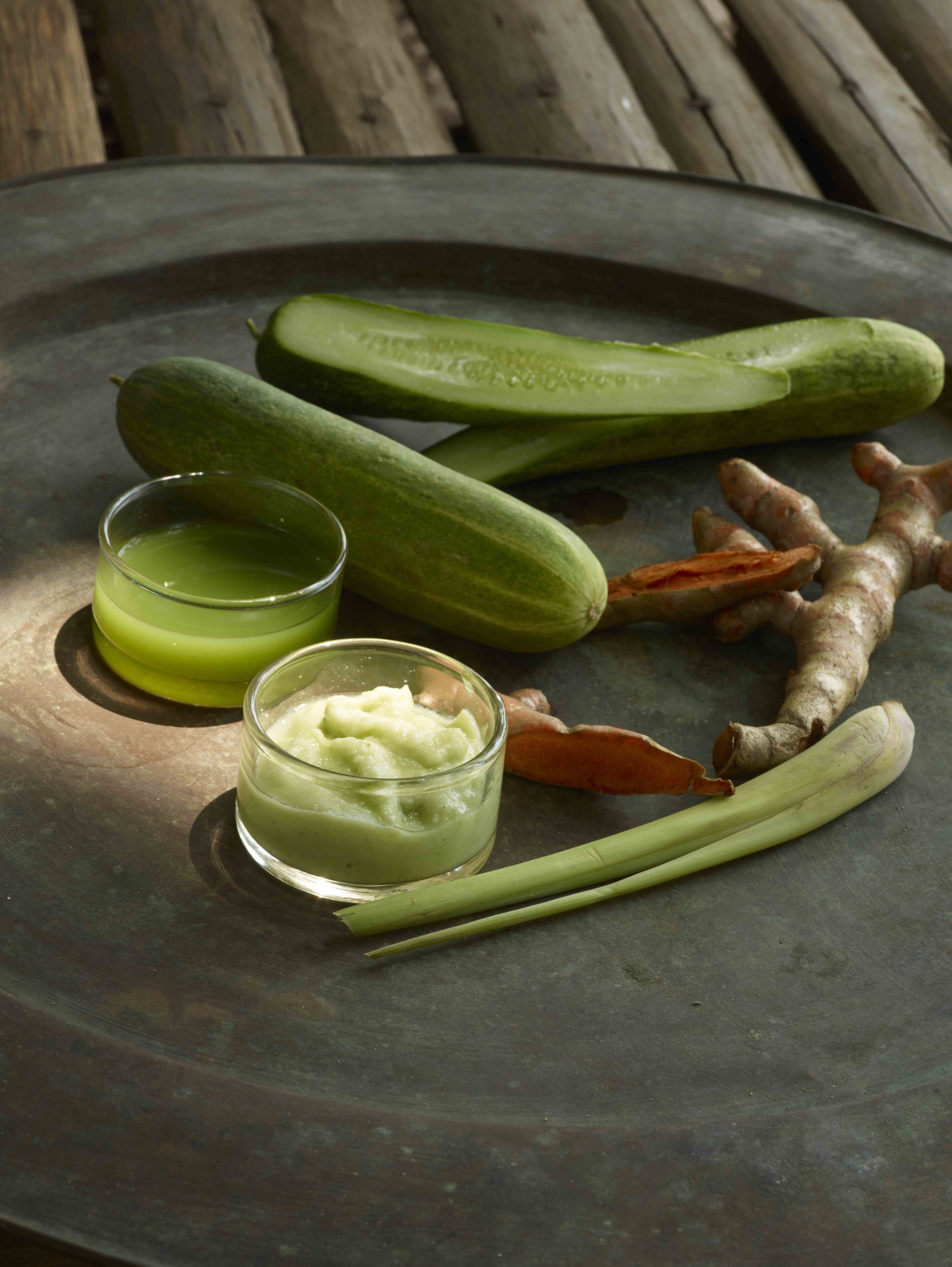 Een metalen dienblad met komkommers, gember en een klein glas groene vloeistof.