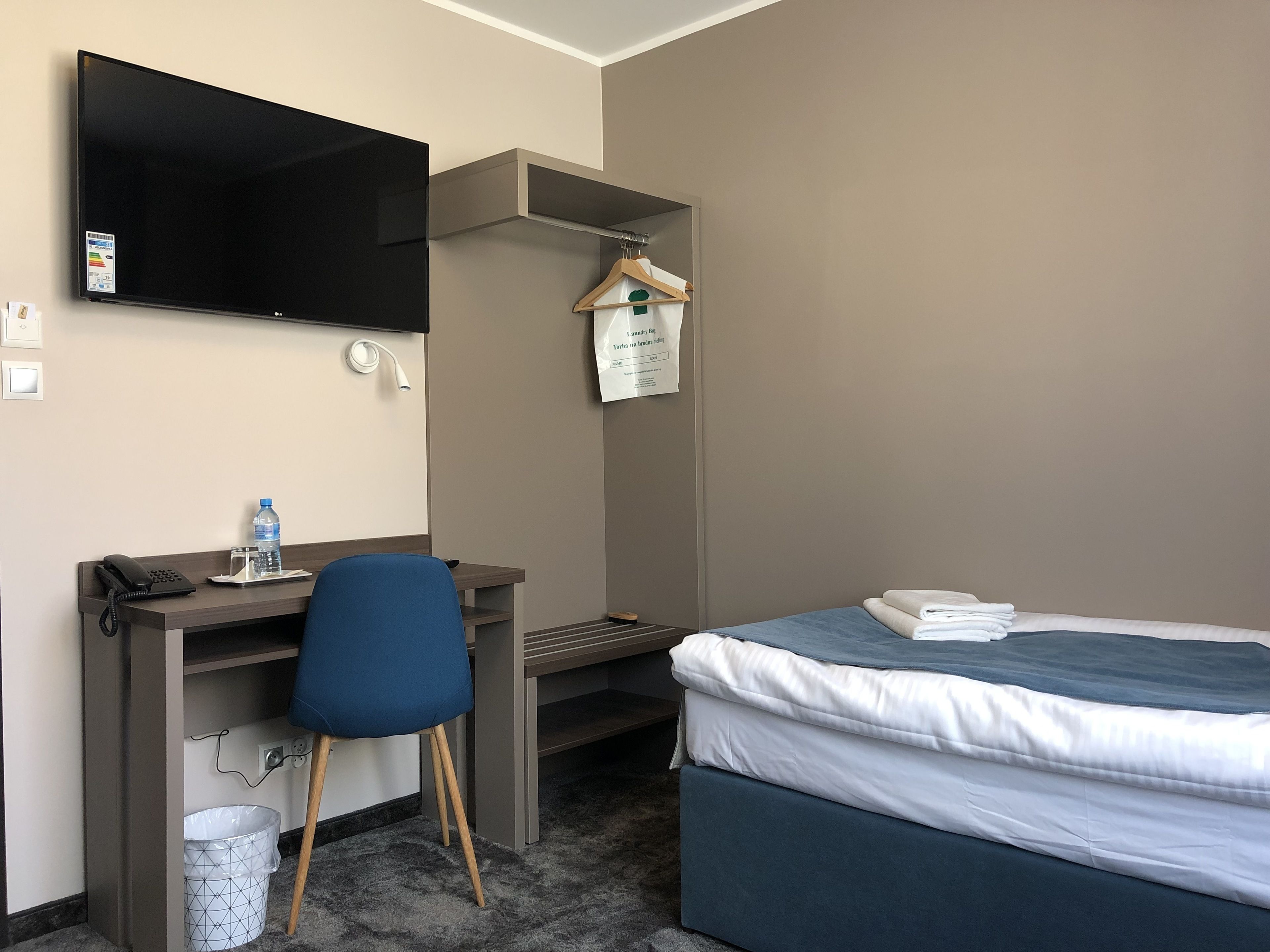 Habitación de hotel con cama, escritorio con silla, televisor, botella de agua y bolsa de lavandería.