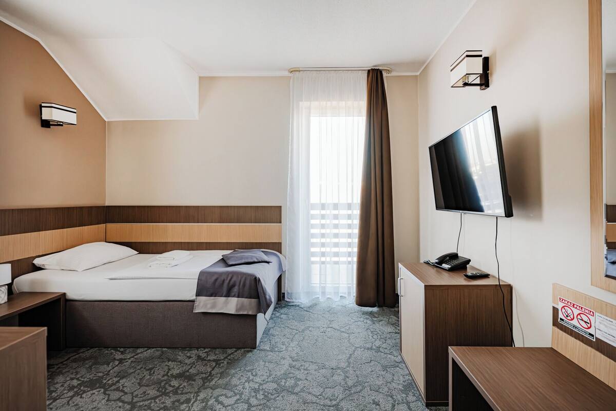 Ett hotellrum med en säng, ett skrivbord, en tv och ett fönster med gardiner.