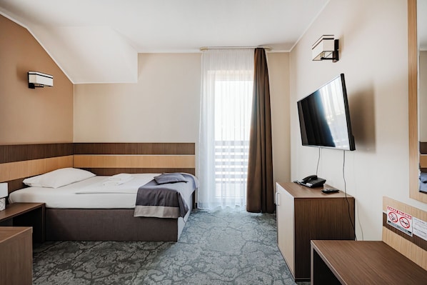 Una habitación de hotel con cama, escritorio, televisión y ventana con cortinas.