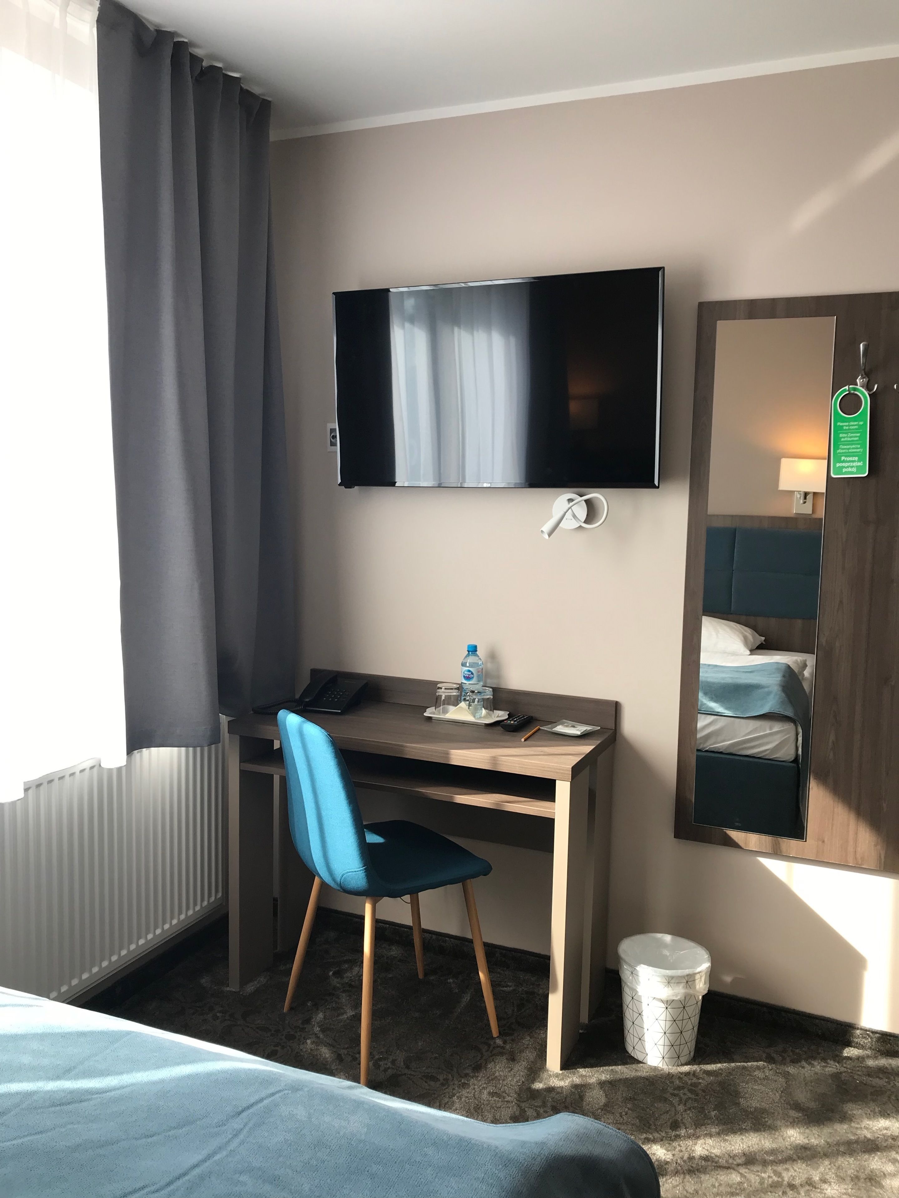 Una habitación de hotel con escritorio, silla, cama, televisor y espejo.