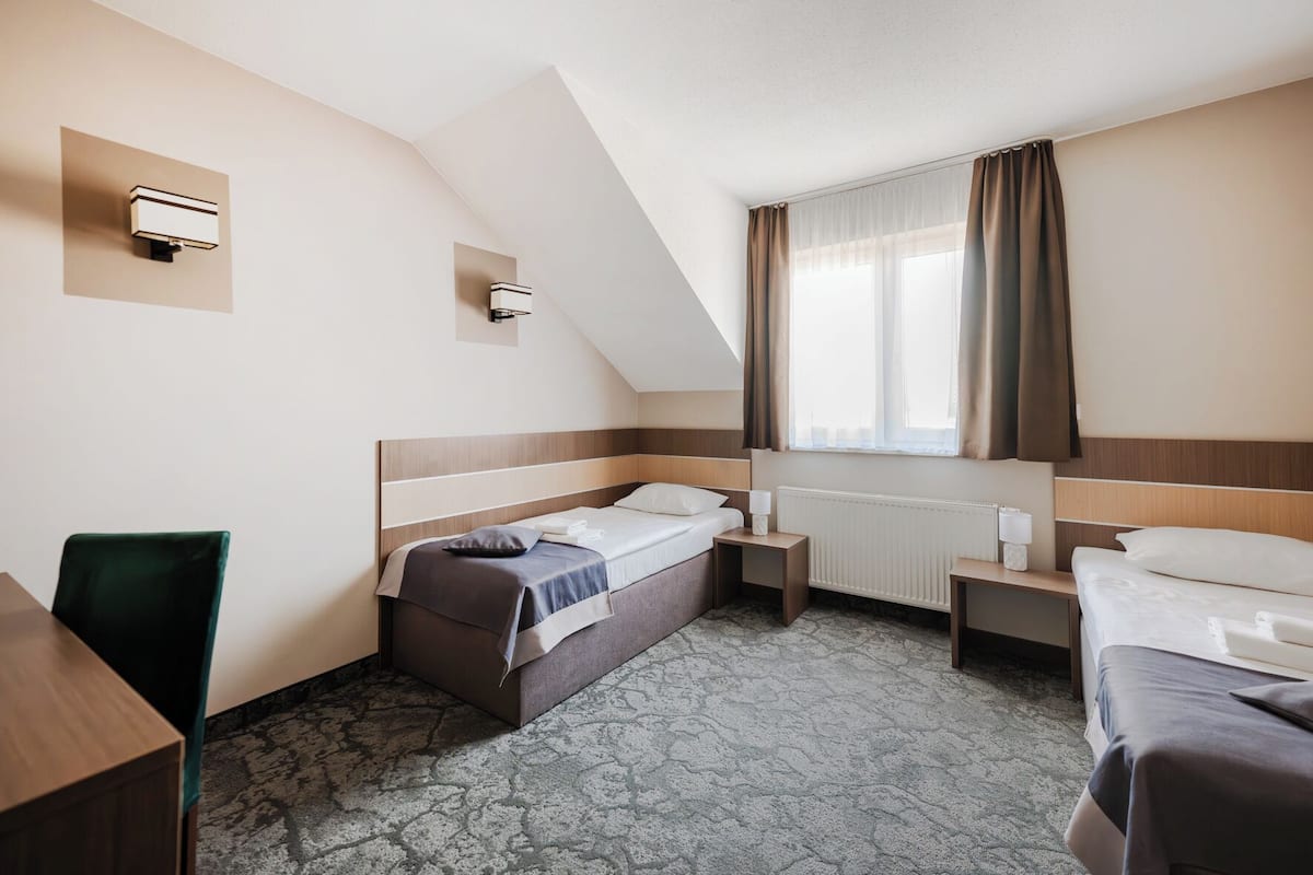 Ett hotellrum med en säng, ett skrivbord, en stol, ett nattduksbord och ett fönster med gardiner.