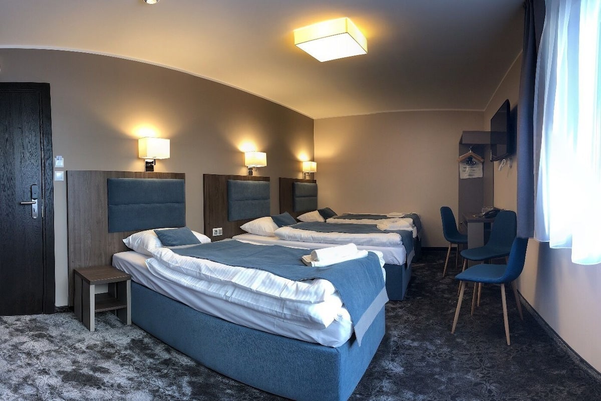 Ett hotellrum med tre sängar, ett skrivbord och två stolar.