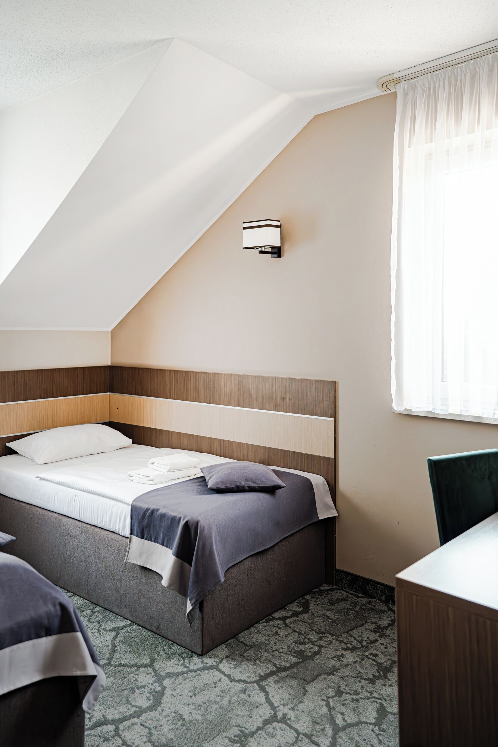 A bedroom with a sloped ceiling, a bed with a wooden headboard, a bedside table, and a chair.