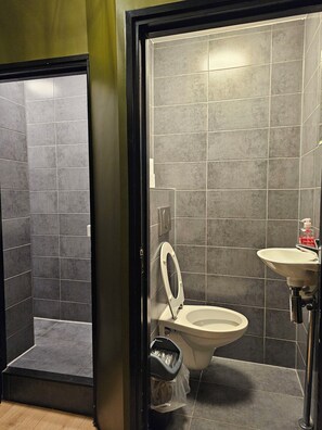 A bathroom with a toilet, a sink, and a trash bin. - Crossroads Hostel Amsterdam (Amsterdam)