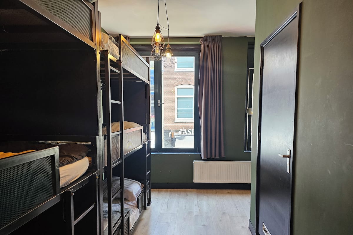 A room with bunk beds, a radiator, a window with curtains, and a door.