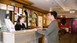 A reception desk with a wooden counter, a clock, and various signs including "RECEPTION" and "CHECK OUT TIME 10am". - Crossroads Hostel Amsterdam (Amsterdam)