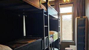 A dormitory room with bunk beds, a small stool, a radiator, and a window with a view of the outside. - Crossroads Hostel Amsterdam (Amsterdam)