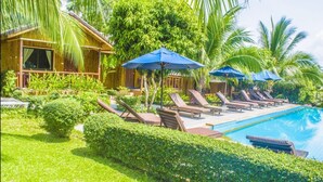 A poolside area with lounge chairs and umbrellas, surrounded by lush greenery and a wooden building. - The Fisherman's Chalet (Koh Samui)