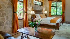 Una habitación con pared de piedra, una cama con manta naranja, techo de madera y una ventana con cortinas naranjas.