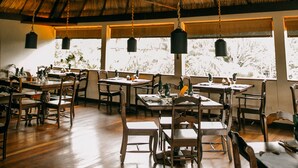 Un restaurante con mesas y sillas de madera, techo de paja y lámparas colgantes.