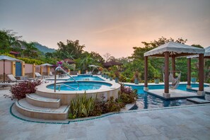 A circular pool with a hot tub, surrounded by lounge chairs and a gazebo.