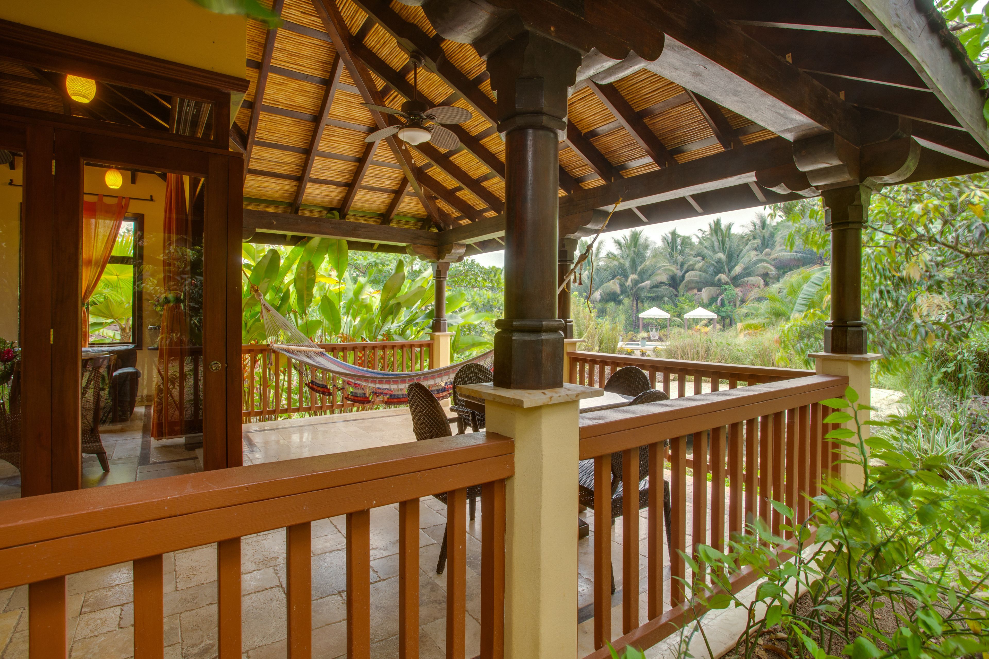 A covered outdoor area with wooden railings, a hammock, and a table with chairs.
