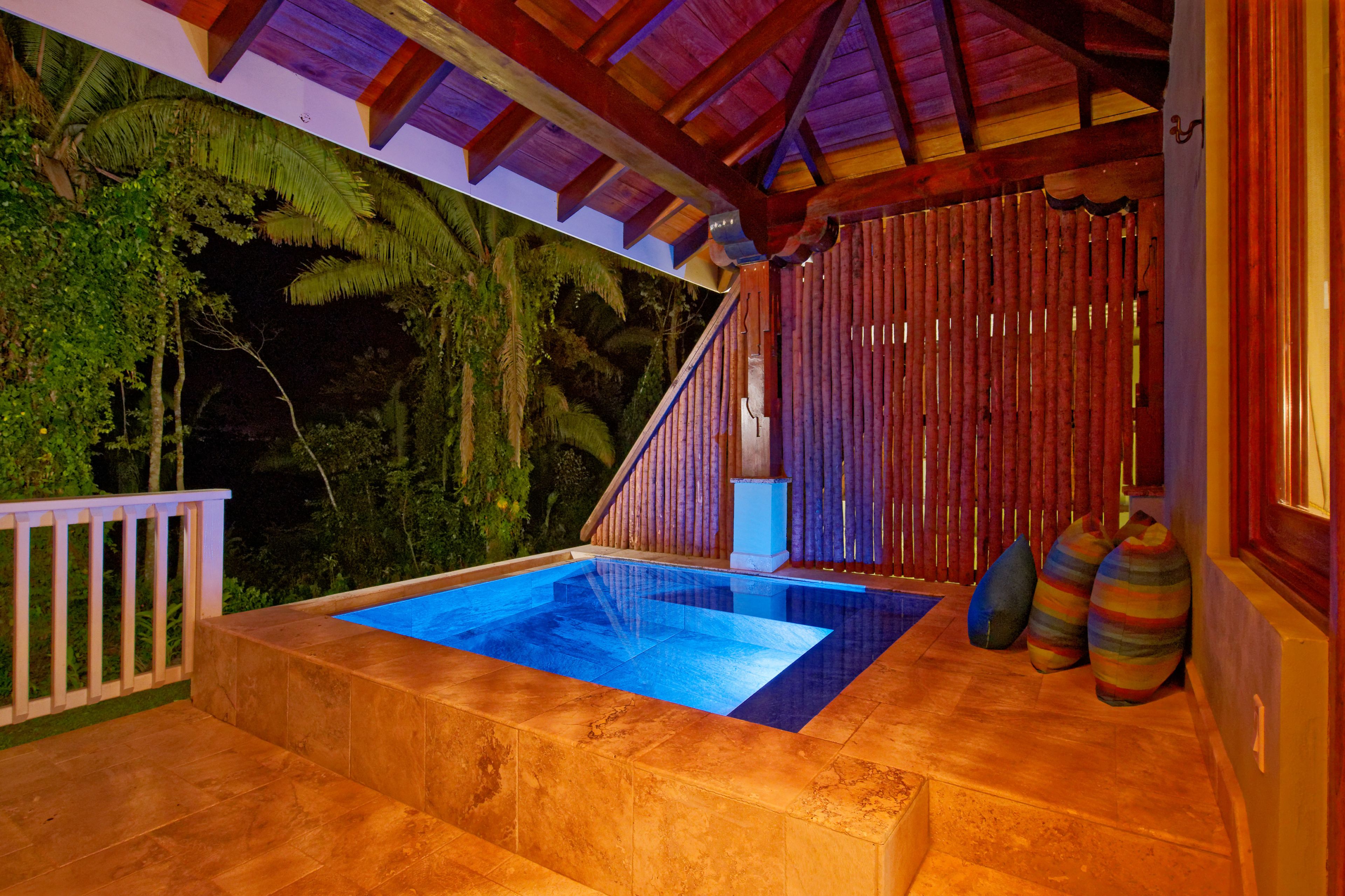 A private pool area with a wooden deck, a small seating area, and a view of tropical foliage.