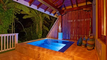 A private pool area with a wooden deck, a small seating area, and a view of tropical foliage.