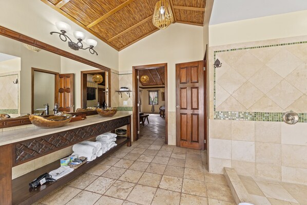 A bathroom with a large mirror, wooden vanity, and a shower area.
