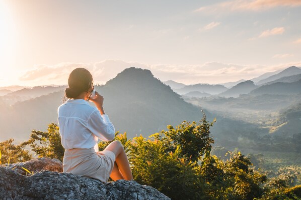 A person sitting on a rock with a mountainous landscape in the background.