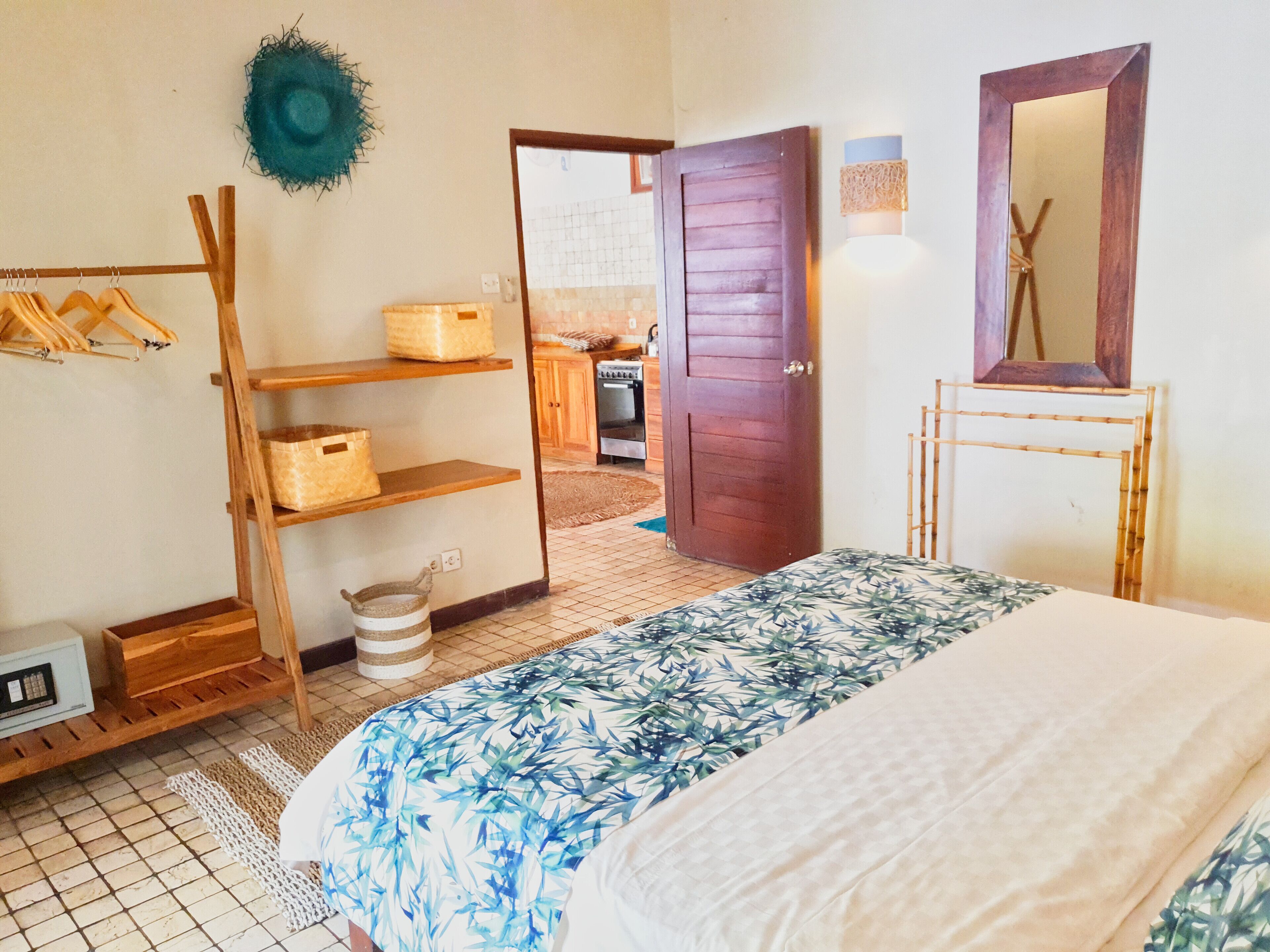 Une chambre à coucher avec un lit, des étagères en bois, un chapeau accroché, un miroir et une porte donnant sur la cuisine.