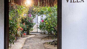 Un sendero lleva a la entrada de una villa con techo de paja y abundante vegetación.