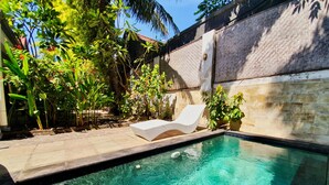 Una piscina con una tumbona blanca y exuberante follaje.