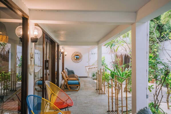 Un espace extérieur aménagé, abrité et doté de chaises en osier et d’un hamac, entouré de plantes en pot et offrant une vue sur le jardin.