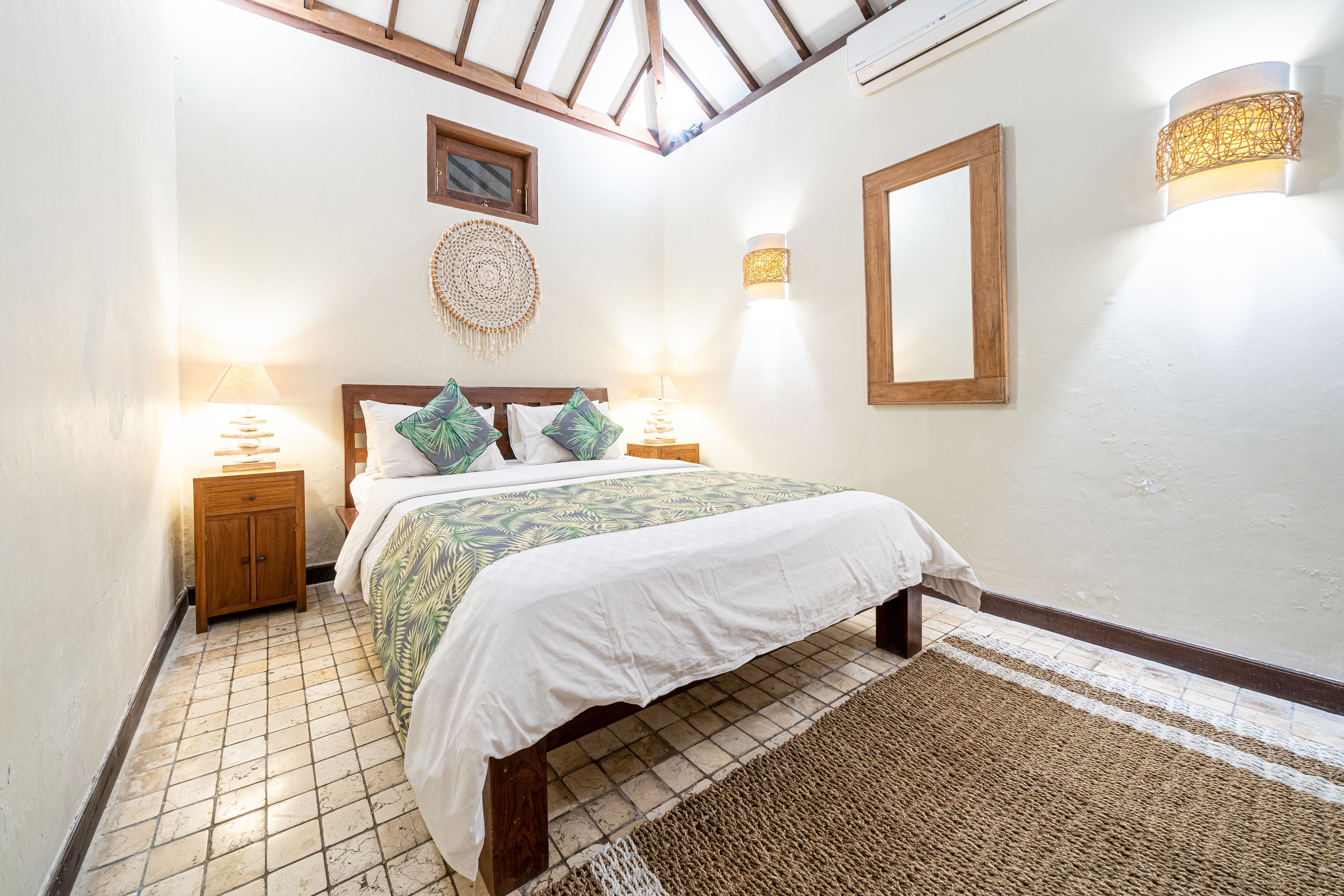 A bedroom with a bed, bedside tables, a wall-mounted mirror, and a ceiling fan.