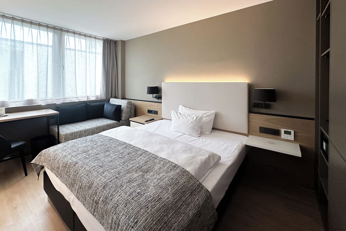 Una habitación de hotel moderna con una cama grande, un escritorio y un sofá.