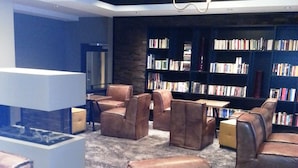 A modern lounge area with leather seating, a fireplace, and a bookshelf filled with books. - Hotel Restaurant Wessinger (Neu-Isenburg)