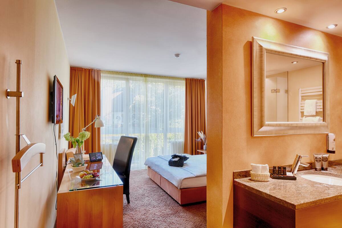 Una habitación de hotel con cama, escritorio, silla y baño con lavamanos y espejo.