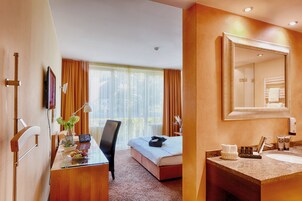Ein Hotelzimmer mit Bett, Schreibtisch, Stuhl und einem Badezimmer mit Waschbecken und Spiegel.