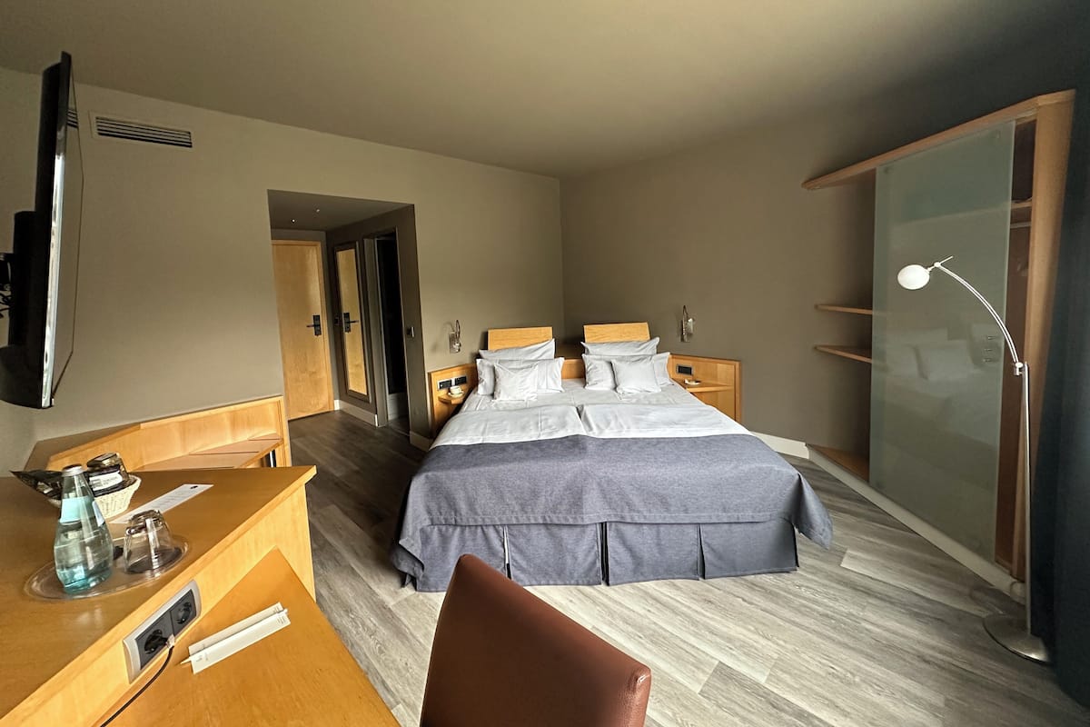 Habitación de hotel con cama, mesitas de noche, un escritorio con silla, televisor y armario.