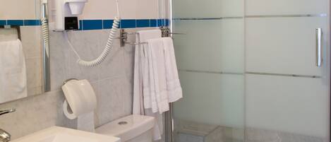 A bathroom with a glass shower enclosure, a white toilet, a sink with a mirror, and a hairdryer mounted on the wall.