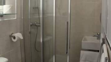 Een badkamer met een douchecabine van glas, een toilet en een wastafel.